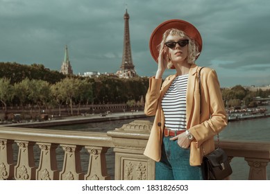 Outdoor Portrait Of Stylish Woman Wearing Autumn Outfit: Orange Hat, Black Cat Eye Sunglasses, Yellow Blazer, Striped T-shirt, Red Belt, Wrist Watch, Posing In Street Of Paris