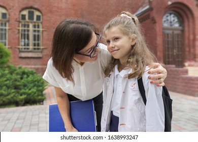 Outdoor portrait of teacher woman and little student girl together. Teacher hugging child near school building. Back to school, start of classes