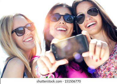Outdoor portrait of three friends taking photos with a smartphone