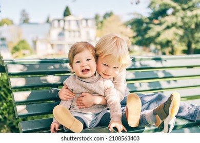 Outdoor Portrait Of Two Adorable Siblings Resting On The Bench In Sunny Park, Preschooler Brother Hugging Sweet Toddler Sister