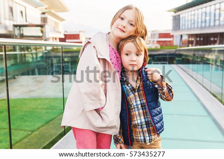 Outdoor portrait of two cute kids, little brother and big sister, boy and girl in a city, wearing spring jackets