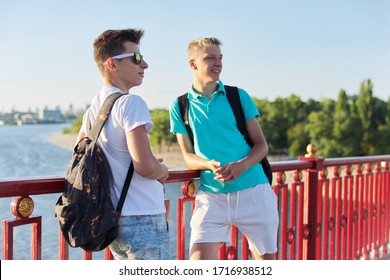 Outdoor Portrait Of Two Friends Boys Teenagers 15, 16 Years Old, Talking Laughing. Guys Standing On Bridge Over River On Sunny Summer Day. Youth, Friendship, Communication