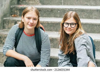 Outdoor portrait of two teenage girl sitting on stairs, wearing backback, looking at the camera