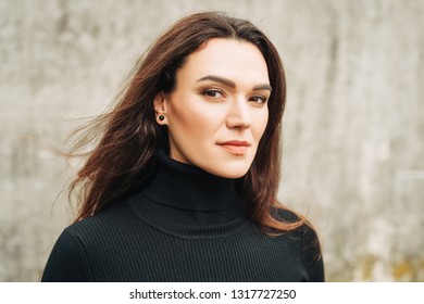 Outdoor portrait of young 35 year old woman with long dark hair, wearing black turtle neck dress