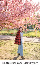 Outdoor portrait of young beautiful Caucasian teen girl smiling and looking into camera, blossom par full of cherry trees on a windy day. 4K footage with sunlight rays