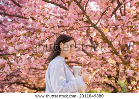 Outdoor portrait of young beautiful Caucasian teen girl smiling and looking into camera, blossom par full of cherry trees on a windy day. 4K footage with sunlight rays