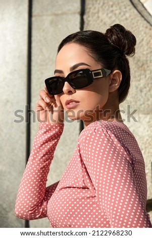 Outdoor portrait of a young beautiful confident woman posing on the street. Model wearing stylish sunglasses. Girl looking up. Female fashion. Sunny day. Close up. City lifestyle. Copy space for text