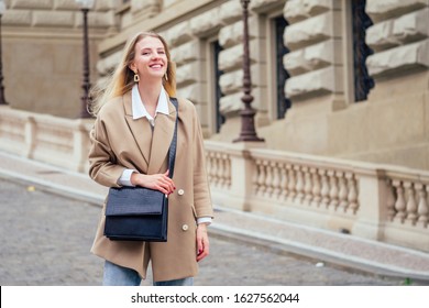 Outdoor portrait of young beautiful fashionable woman wearing trendy jacket with small shoulder bag, walking in street of european Chezh Praha city