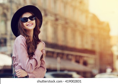 Outdoor portrait of a young beautiful fashionable happy lady posing on a street of the old city. Model wearing stylish clothes. Girl looking up. Female fashion. City lifestyle. Copy space for text - Powered by Shutterstock