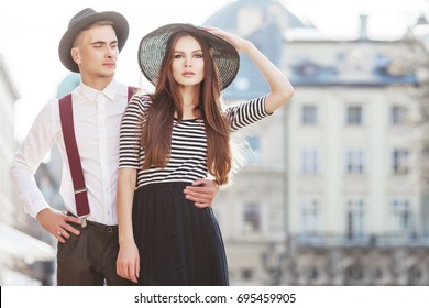 Outdoor Portrait Of Young Beautiful Fashionable Couple. Man And Woman Posing In Street. Models Wearing Stylish Clothes And Accessories. Sunny Day Light. Fashion Concept. Copy, Empty Space For Text
