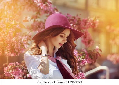 Outdoor portrait of young beautiful happy smiling lady posing near flowering tree. Model wearing stylish accessories & clothes. Girl closed her eyes. Female beauty & fashion concept. City lifestyle - Powered by Shutterstock