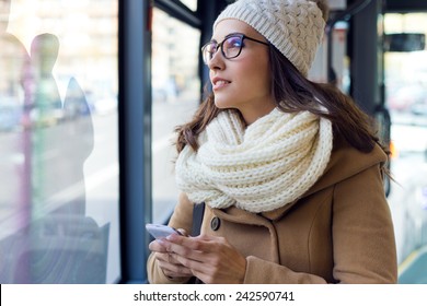 Outdoor portrait of young beautiful woman using her mobile phone on a bus.