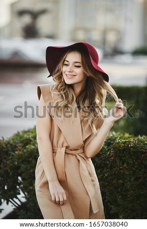 Outdoor portrait of a young beautiful woman with long platinum blond hair in modish outfit. Model girl in stylish coat and trendy hat. Female fashion, beauty concept