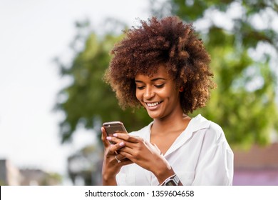 Außenporträt einer jungen schwarzen Afroamerikanerin, die auf dem Handy spricht