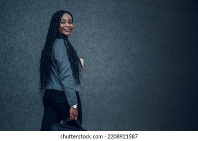 Outdoor Portrait Of Young Confident African American Business Woman In Formal Clothes Holding Business Bag And A Coffee Cup And Smiling At Camera. Waiting For A Business Meeting Outside Of The Office.