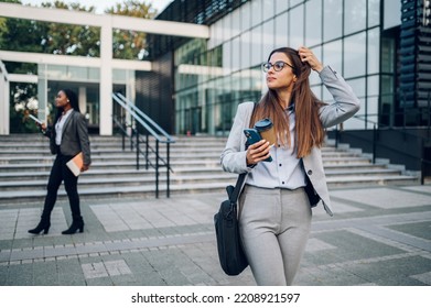 Outdoor Portrait Of Young Confident Beautiful Business Woman In Formal Clothes Fixing Her Hair And Holding Coffee Takeaway And Smartphone . Waiting For A Business Meeting Outside Of The Office.