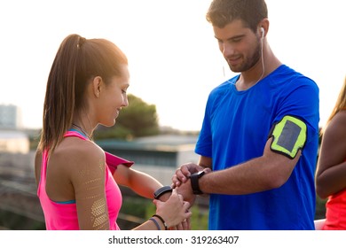 Outdoor Portrait Of Young Couple Using They Smartwatch After Running.