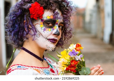 outdoor portrait of young latin caucasian woman, with face painted as La Calavera catrina, standing on blurred cemetery in background and copy space.