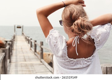 Outdoor portrait of young pretty blonde sexy tanned woman standing on the pier near the sea and waiting for somebody alone 