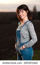 An Outdoor Portrait Of A Young Woman Smiling And Wearing Dungarees In The Countryside