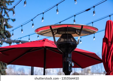 Outdoor Propane Heater Below Strand Lights And Patio Umbrellas With Space For Text On The Left