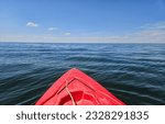 Outdoor recreation image of the bow of a red kayak floating on the water and pointed towards the vast empty body of water and the horizon over water.