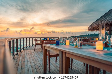 Outdoor restaurant at the beach. Table setting at tropical beach restaurant. Led light candles and wooden tables, chairs under beautiful sunset sky. Luxury hotel or resort restaurant - Powered by Shutterstock