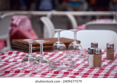 Outdoor restaurant patio table set with red checkered table cloth and wine glasses - Powered by Shutterstock