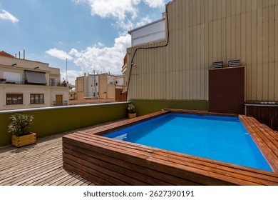 Outdoor rooftop area with elevated rectangular blue pool surrounded by wooden deck and potted plants