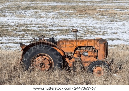 Outdoor rural scene of an antique tractor at the edge of an agricultural field with a light dusting of snow and dry grass.