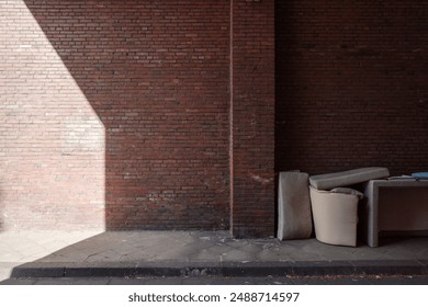 An outdoor scene featuring an abandoned pile of furniture against a weathered red brick wall. - Powered by Shutterstock