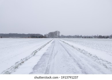 Outdoor Scenery Diminishing Perspective View On Street Along Land And Field Covered With Thick Layer Snow And Background Of Cloudy Overcast Sky In Countryside In Germany During Winter Season.