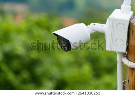 Outdoor security camera mounted on a wooden post with green foliage in the blurred background