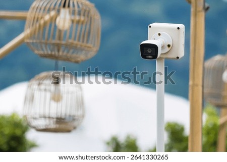 Outdoor security camera mounted on a wooden post with green foliage in the blurred background