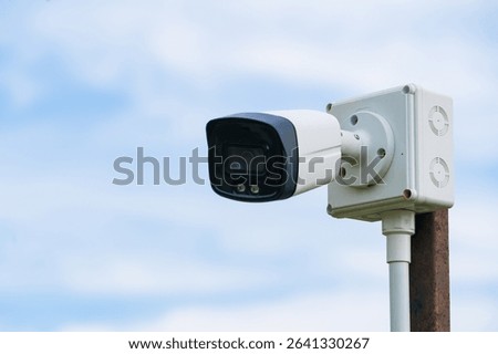 Outdoor security camera mounted on a wooden post with green foliage in the blurred background