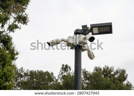 Outdoor security camera mounted on a pole near trees. Captures surroundings for safety and surveillance purposes in a tropical environment. Enhances security measures