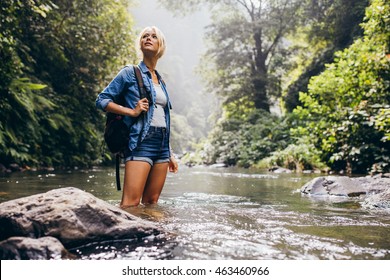 Outdoor shot of attractive young woman with backpack standing in a wilderness stream. Caucasian female hiker in creek water.