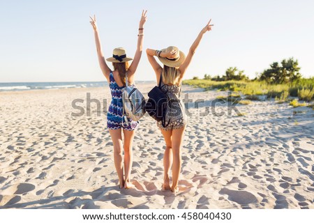Outdoor shot of cheerful young female friends are back with their hands raised together on a beach at sunset . Two attractive women enjoying a holiday on the sea shore.