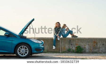 Outdoor shot of couple of travelers sitting near the broken car with open hood, Man and woman looking tired, frustrated while waiting for assistance or tow truck, Web Banner