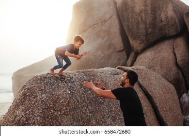 Outdoor shot of father and son having fun on summer holidays at the beach. happy little boy jumping into his father's arms from a rock.