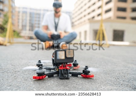 Outdoor shot of fpv multicopter drone landing on the street road with the male pilot operating on the background. Focus is on copter.