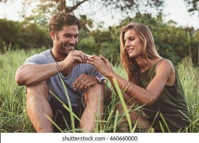 Outdoor shot of man placing ring on finger of young woman. Man proposing to girlfriend.