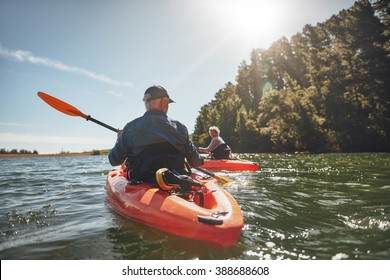 Outdoor shot of mature man canoeing in the lake with woman in background. Couple kayaking in the lake on a sunny day. - Powered by Shutterstock