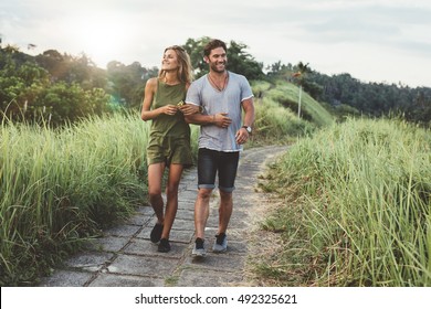 Outdoor shot of young couple in love walking on pathway through grass field. Man and woman walking along tall grass field.