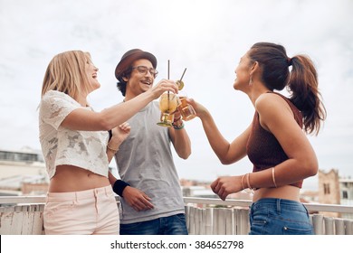 Outdoor Shot Of Young People Enjoying Cocktails At A Party. Three Young Friends Toasting Drinks During Rooftop Party.