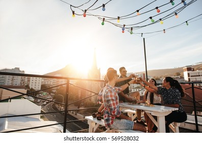 Outdoor shot of young people toasting drinks at a rooftop party. Young friends hanging out with drinks. - Shutterstock ID 569528032