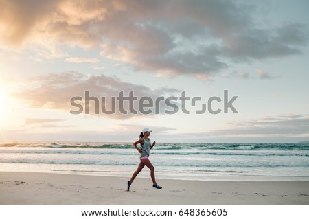 Outdoor shot of young sports woman running along the sea shore in morning. Fitness female doing running exercise on the beach.