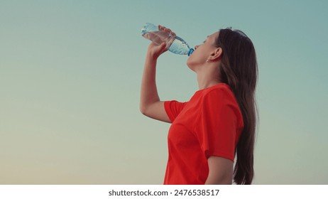 Outdoor sports, girl drinks clear mineral water after training at sunset in sun. Quench your thirst with cool water. Young Woman drinks refreshing water from bottle after training in park in nature - Powered by Shutterstock