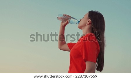 Outdoor sports, girl drinks clear mineral water after training at sunset in sun. Quench your thirst with cool water. Young Woman drinks refreshing water from bottle after training in park in nature 商業照片 © 