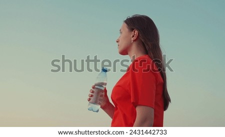 Outdoor sports, girl drinks clear mineral water after training at sunset in sun. Quench your thirst with cool water. Young Woman drinks refreshing water from bottle after training in park in nature